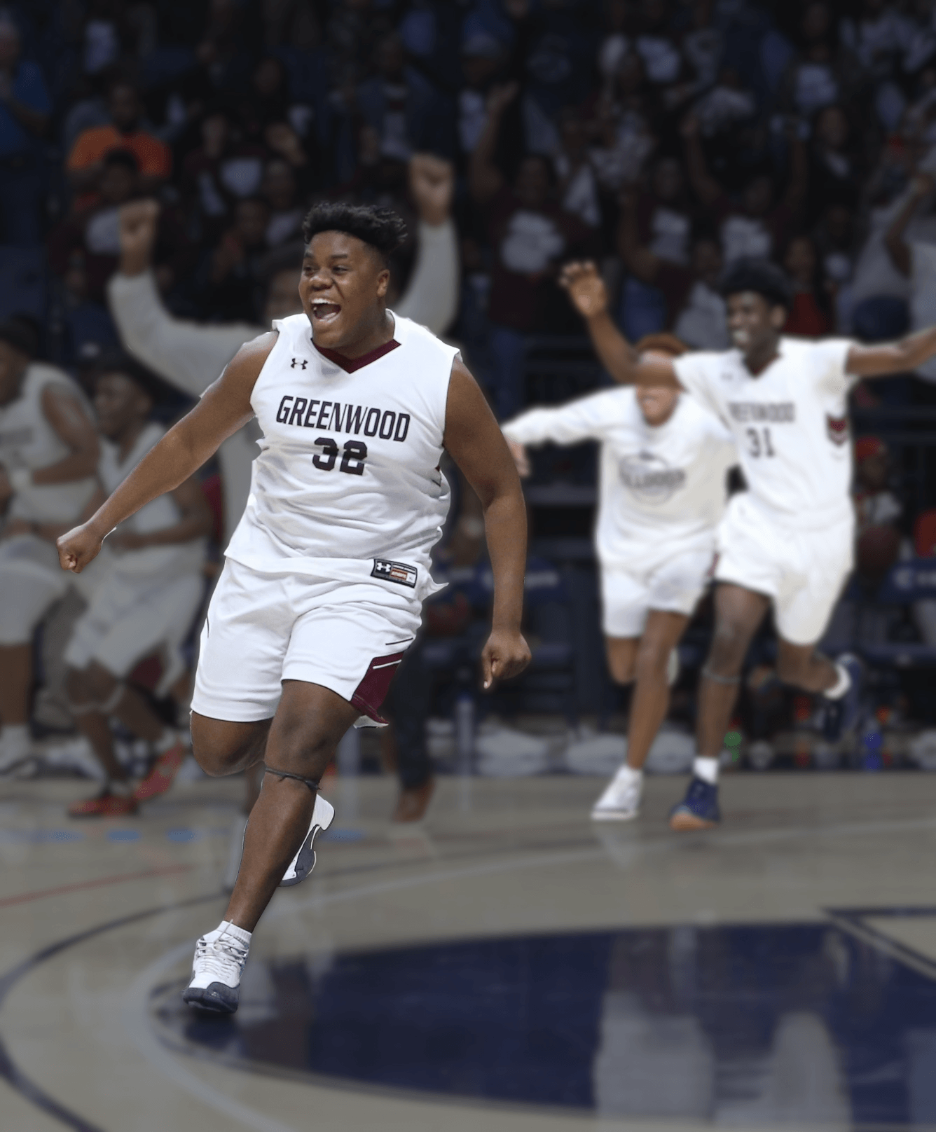A boys basketball player running in the court in celebration. Two teammates are behind him celebrating. 